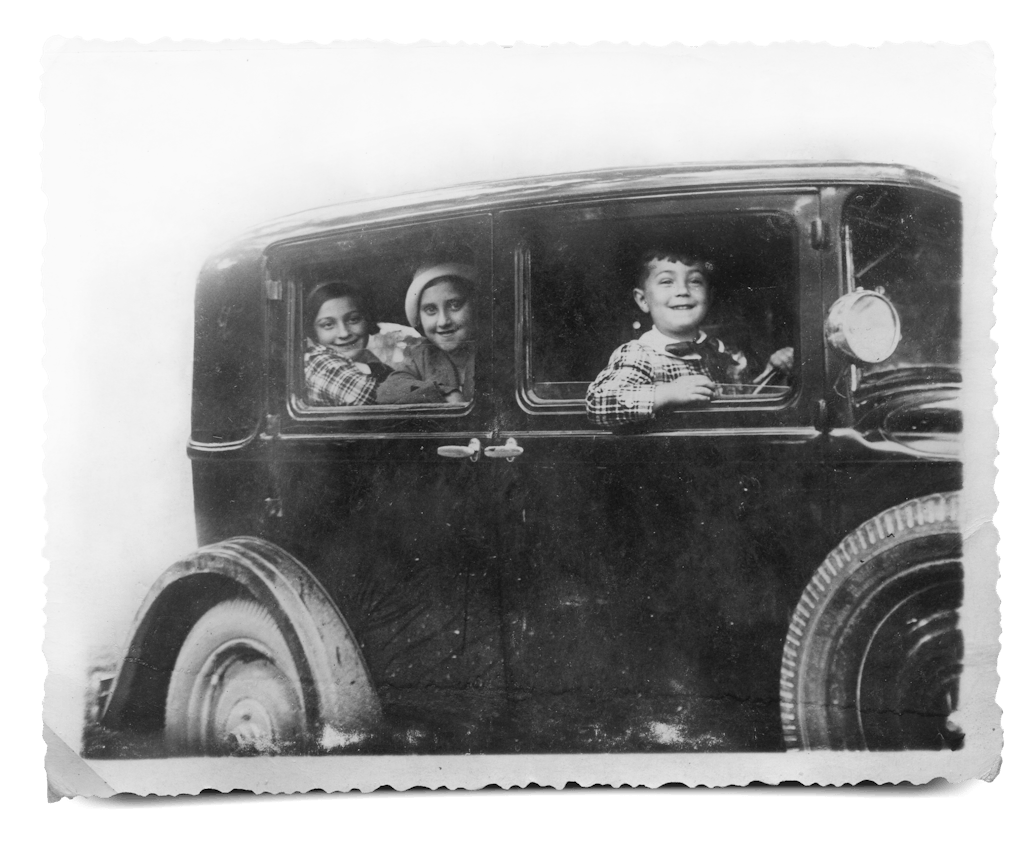 Iby, Trudi and Tomy grinning from the windows of a classic car in 1932